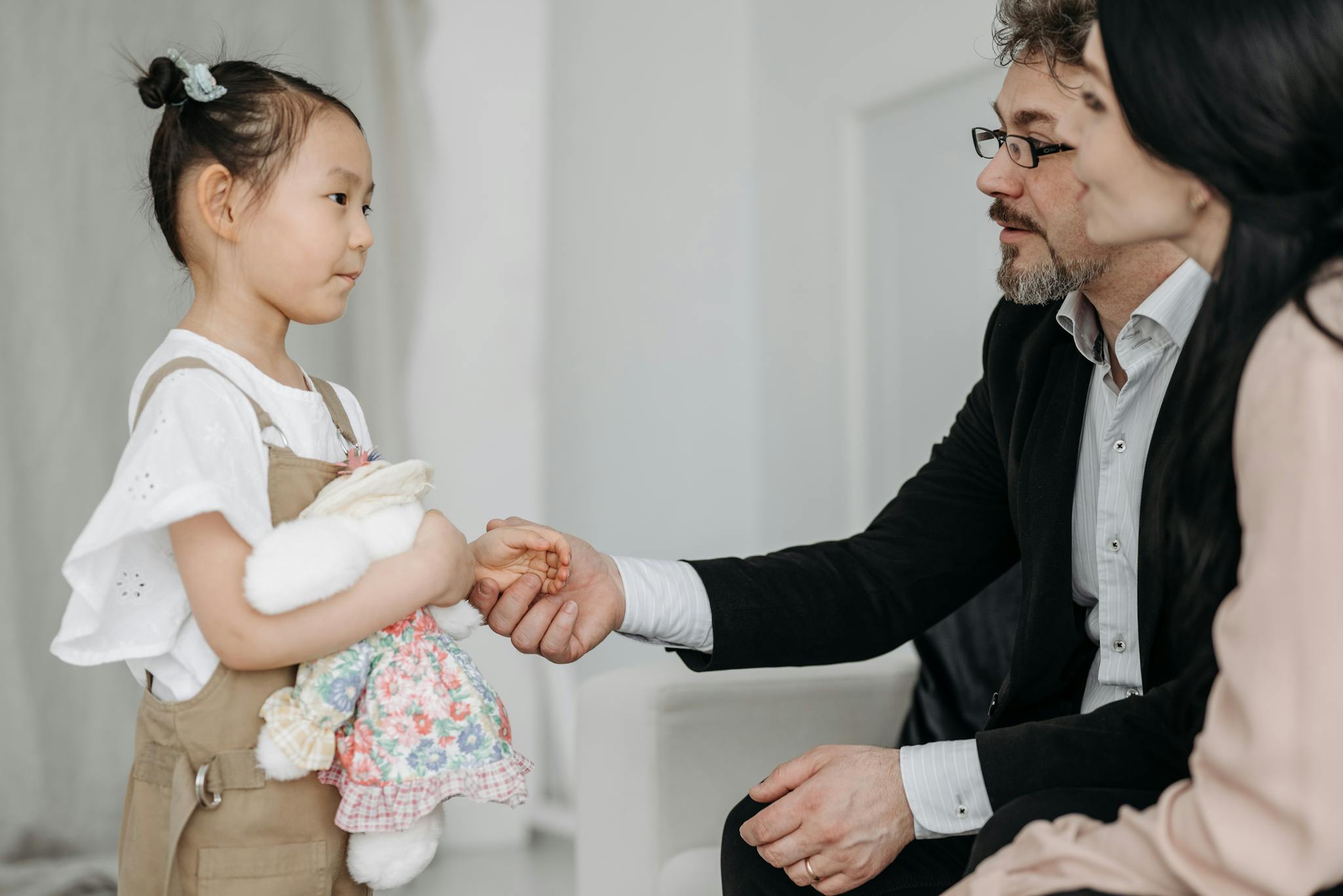 A joyful moment of a couple adopting a young Asian girl holding a teddy bear indoors.
