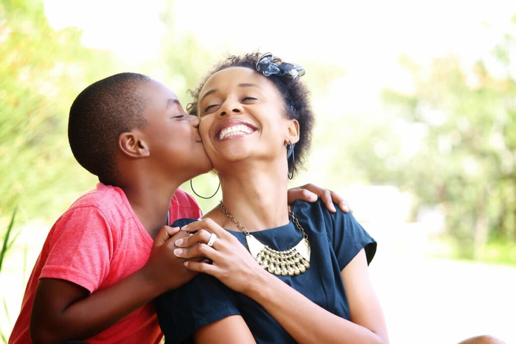African boy kisses his smiling mother on the cheek – joyful modern parenting moment